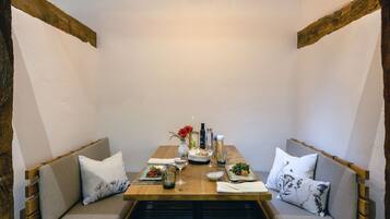 A cozy dining area with a wooden table set for two, surrounded by cushioned benches with pillows.