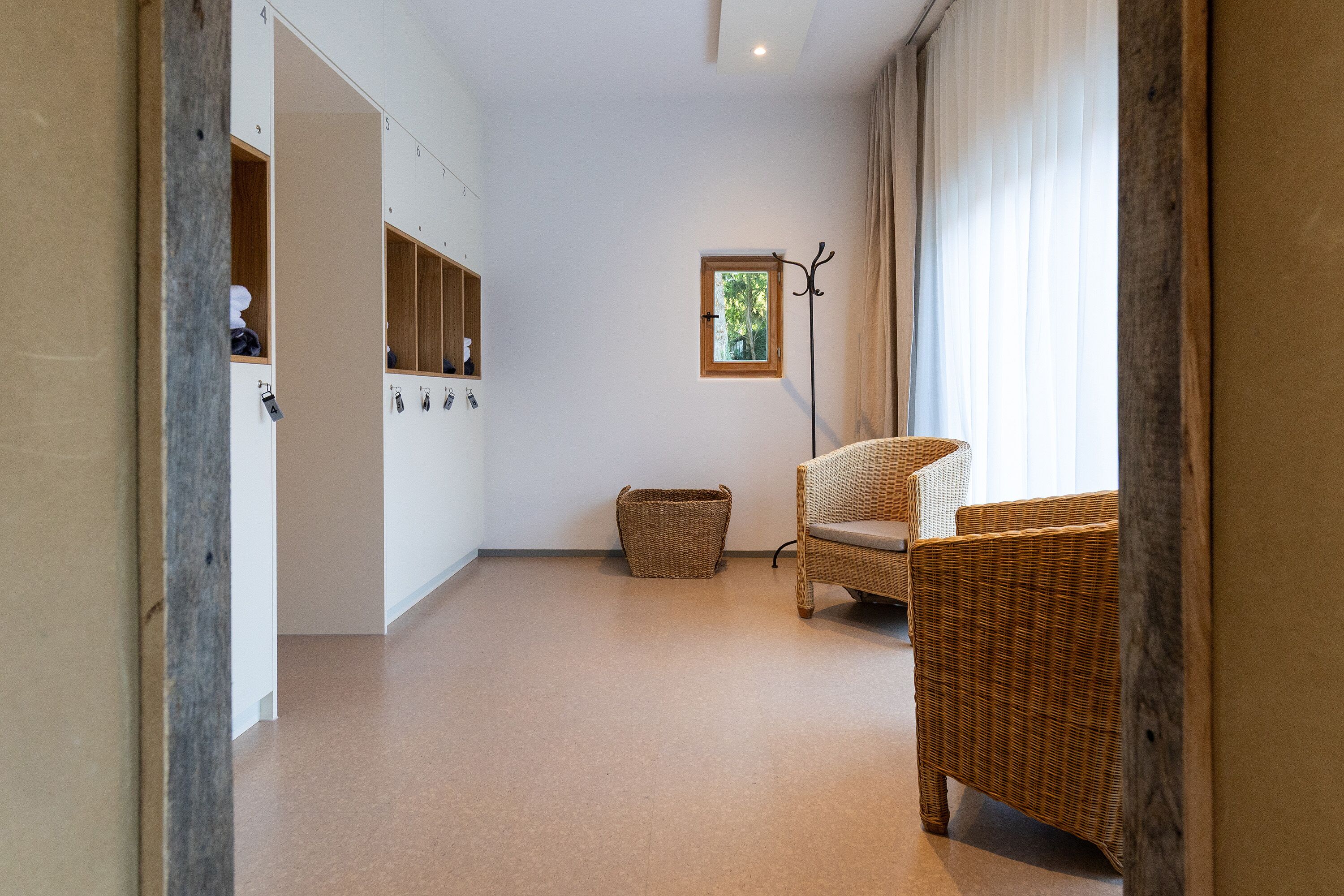 A room with a wicker chair, a small window, and a coat rack.