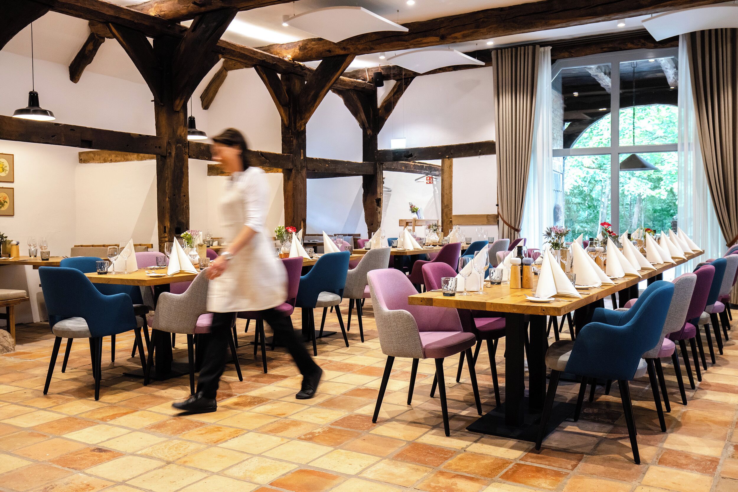Un restaurante con vigas de madera, suelo de baldosas y varias mesas con sillas.