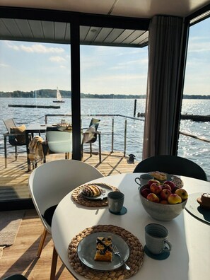 Un comedor con una mesa preparada para dos personas, un frutero, un plato con una porción de pastel y una taza.