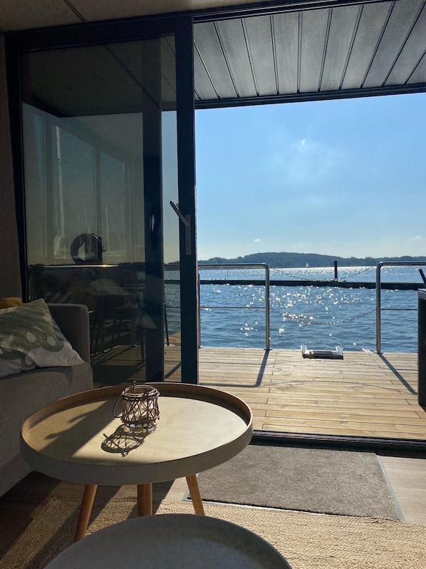 A modern room with a large sliding glass door leading to a deck overlooking a body of water.