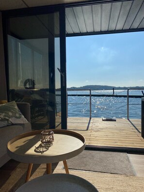 Ein moderner Raum mit einer großen Schiebeglasdoor, die auf eine Terrasse mit Blick auf ein Gewässer führt.