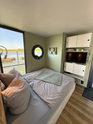 Een slaapkamer met een bed, een televisie, een rond raam en uitzicht op het water.