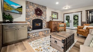 A living room with a stone fireplace, a mounted TV, and a large window. - Mt. Index Riverside with hot tub, wifi, grill, fireplace and more! (Gold Bar)