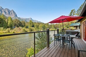 A deck with outdoor seating and a red umbrella, overlooking a river and mountains. - Mt. Index Riverside with hot tub, wifi, grill, fireplace and more! (Gold Bar)