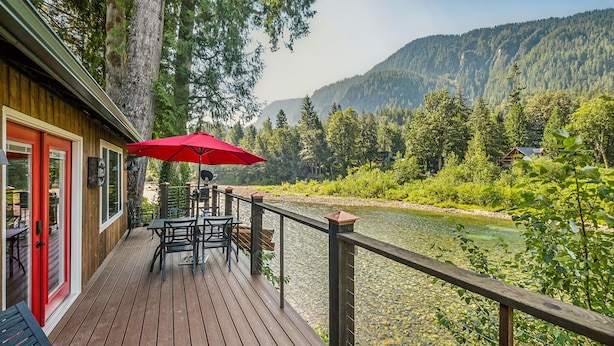 A wooden deck with outdoor seating, overlooking a river and forested mountains. - Mt. Index Riverside with hot tub, wifi, grill, fireplace and more! (Gold Bar)