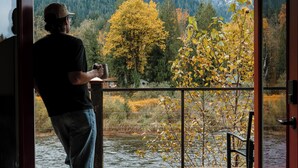 A person standing at a glass door, looking out at a wooden deck with a view of a river and autumn foliage. - Mt. Index Riverside with hot tub, wifi, grill, fireplace and more! (Gold Bar)