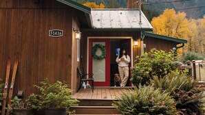 A wooden cabin with a sign reading '51416' at the entrance, surrounded by ferns and a mountain backdrop. - Mt. Index Riverside with hot tub, wifi, grill, fireplace and more! (Gold Bar)