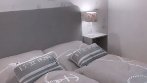 Une chambre à coucher avec un lit, des oreillers, une table de chevet, une lampe et un mur recouvert d’un papier peint représentant des voiliers.