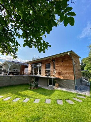 A modern wooden house with a covered patio, a small garden, and a clear blue sky. - New, modern vacation home with a stunning view in the countryside (Mücke)