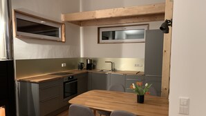 Une cuisine compacte dotée d’un plan de travail en bois, d’un four encastré, d’un évier et d’une fenêtre située au-dessus du plan de travail. On y trouve une table à manger avec deux chaises et un vase rempli de fleurs.