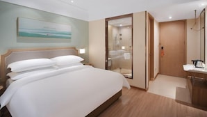 A hotel room with a large bed, a bathroom with a glass shower enclosure, and a small desk with a kettle. - Vienna 3 Best Hotel (Hangzhou)