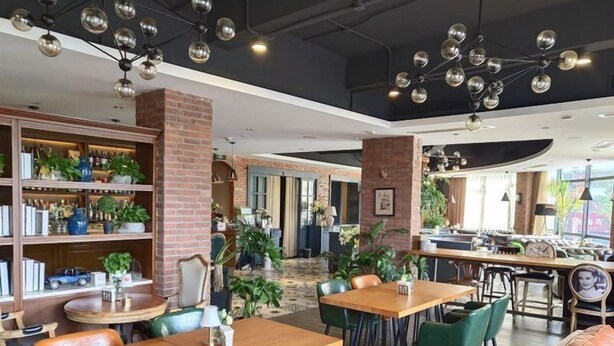 A spacious cafe with wooden tables and chairs, a brick wall, and a variety of plants. - Vienna 3 Best Hotel (Hangzhou)