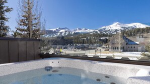 A hot tub with a view of snow-covered mountains and a parking lot.