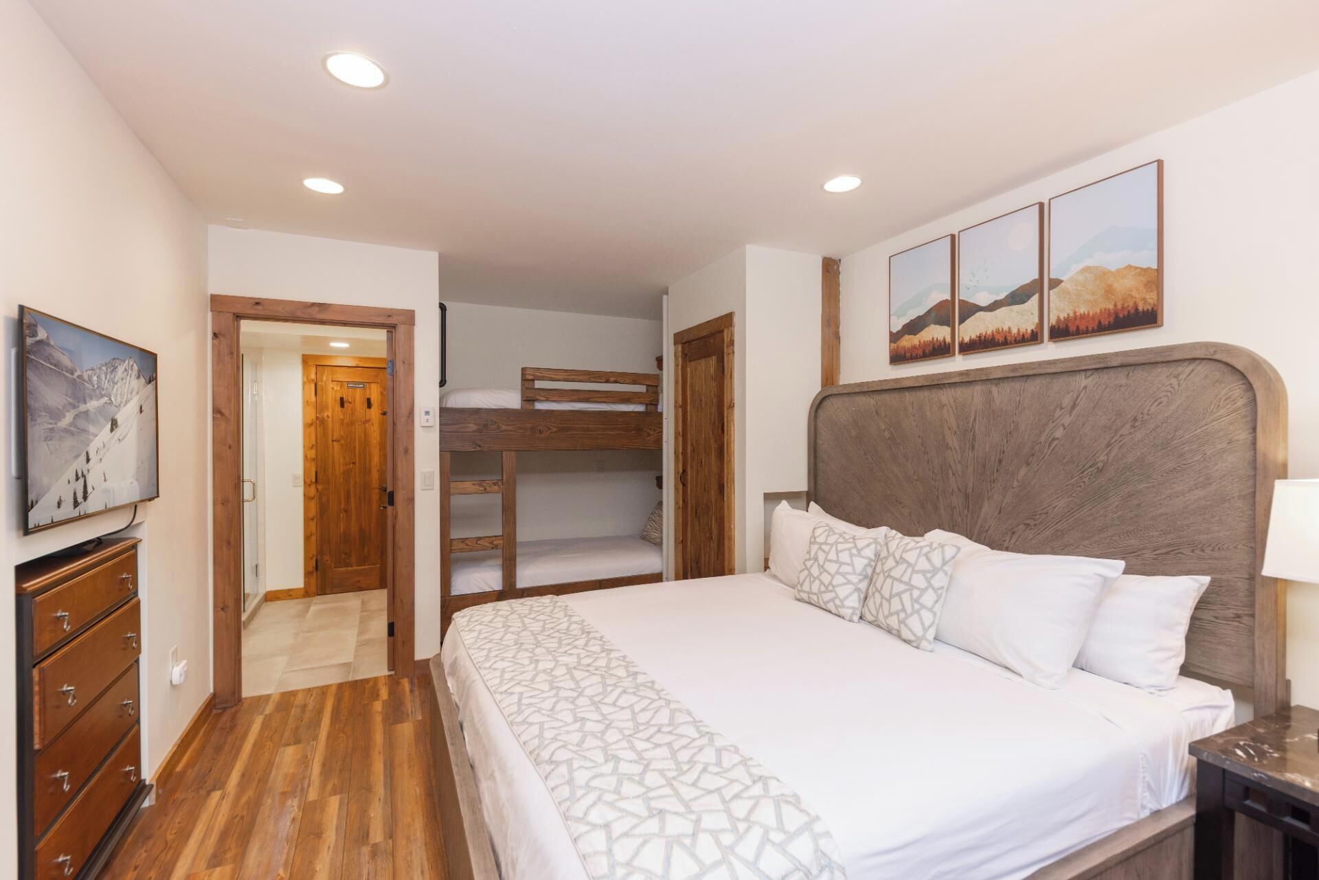 A bedroom with a bunk bed, a large bed with patterned bedding, wooden furniture, and a painting on the wall.
