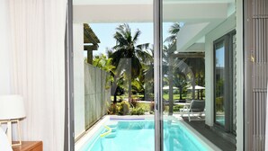 Una habitación de hotel moderna con una puerta de vidrio que da a una zona de piscina privada, con vistas despejadas a palmeras y un jardín bien cuidado.