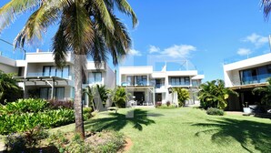 Un hotel moderno con varias construcciones blancas, un césped cuidado y palmeras.