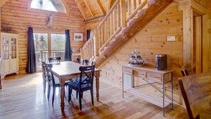 Interior de una cabaña de madera con comedor, escalera y zona de cocina.