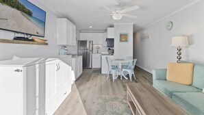 Eine moderne Küche mit weißen Schränken, ein Essbereich mit rundem Tisch und Stühlen, ein Deckenventilator und eine Leuchte.