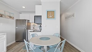 Eine Küche mit weißen Schränken, einem Edelstahl-Kühlschrank, einem runden Tisch mit Stühlen und einem Schild mit der Aufschrift 'BEACH HOUSE'.
