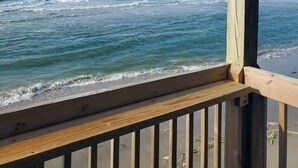 Eine Holzterrasse mit Blick auf einen Strand und Wellen im Meer.
