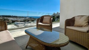 Un balcon agrémenté de meubles en osier, d’une table en verre et offrant une vue sur la ville et la mer.