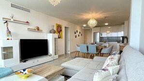 Un salon moderne doté d’un téléviseur à écran plat, d’un canapé, d’un coin repas et d’une cuisine en arrière-plan.