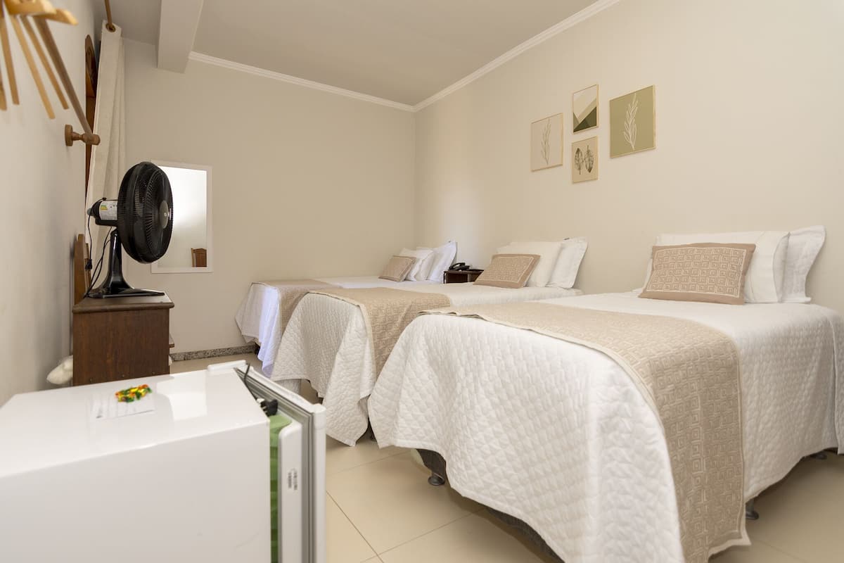 A hotel room with two beds, a bedside table, a fan, and a small refrigerator.