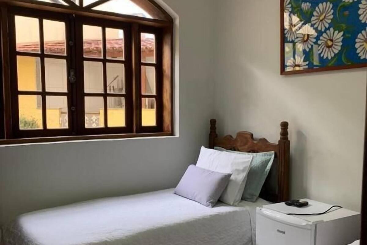 A bedroom with two single beds, a nightstand, a small refrigerator, and a window with a view.