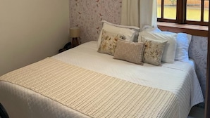 A bedroom with a large bed, a hanging light fixture, a window with curtains, and two framed pictures on the wall. - Pousada Capim Limão (Diamantina)