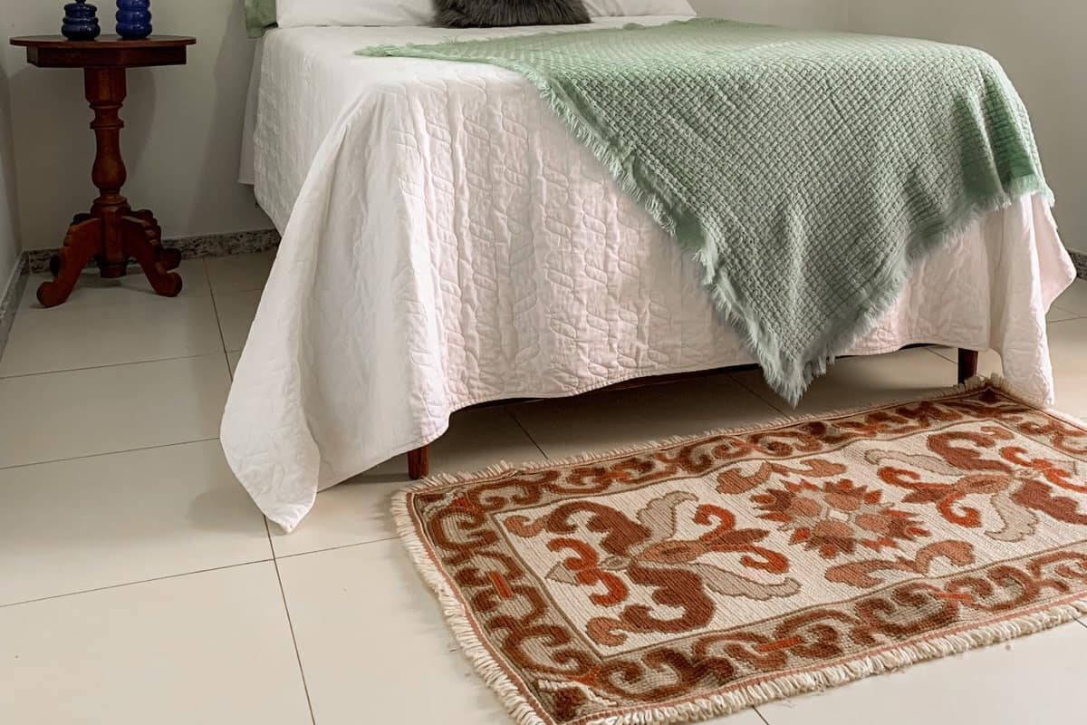 A bedroom with a bed, a bedside table with decorative items, a patterned rug, and a framed picture on the wall.