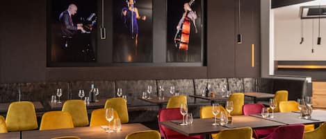 Un restaurante con sillas amarillas y rojas, mesas con copas de vino y tres cuadros en la pared.