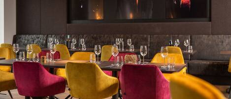 A restaurant with tables set for dining, featuring yellow and red chairs, and a large screen displaying musicians.