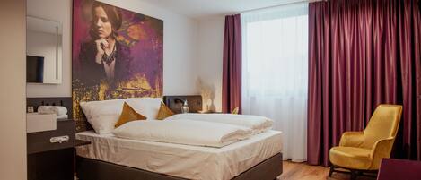 A modern hotel room with a large bed, a desk with a chair, a large window with curtains, and a painting on the wall.