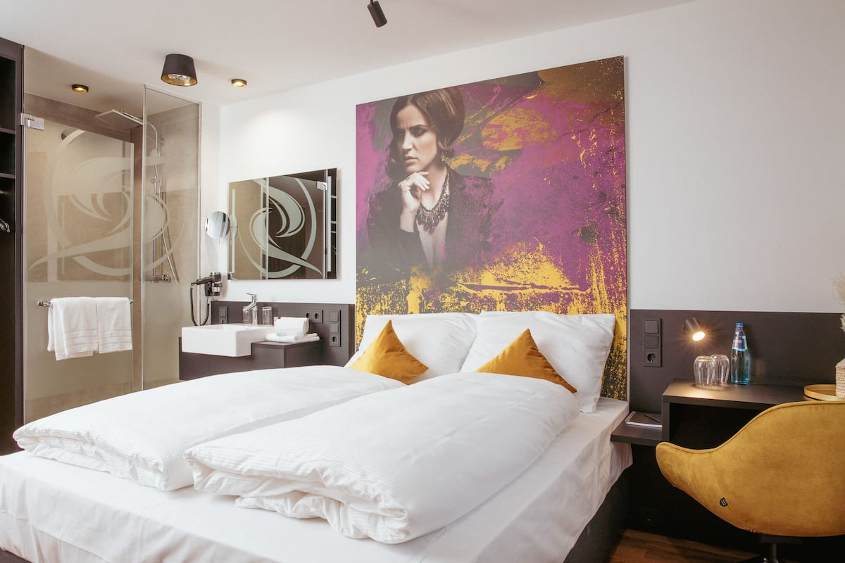 Ein Hotelzimmer mit Bett, einem großen Gemälde, einem Badezimmer und einem Schreibtisch mit Stuhl.