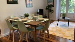 A dining area with a wooden table set for four, surrounded by green chairs. There are two framed posters on the wall, a potted plant on the windowsill, and a small table with a plant. - #CD L' Ainé 👨‍👩‍👦‍👦| Jean Jaurès | Tramway A, B and E| T3 équipé (Grenoble)