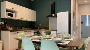 A modern kitchen with white cabinets, a microwave, and a black range hood. There is a dining table set with plates, glasses, and a potted plant. - #CD L' Ainé 👨‍👩‍👦‍👦| Jean Jaurès | Tramway A, B and E| T3 équipé (Grenoble)