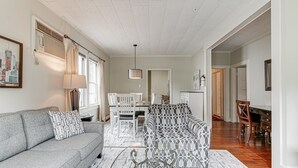 Een ruime woonkamer met een grijze bank, gestreepte kussens, een eettafel met stoelen en een gekleurd vloerkleed.