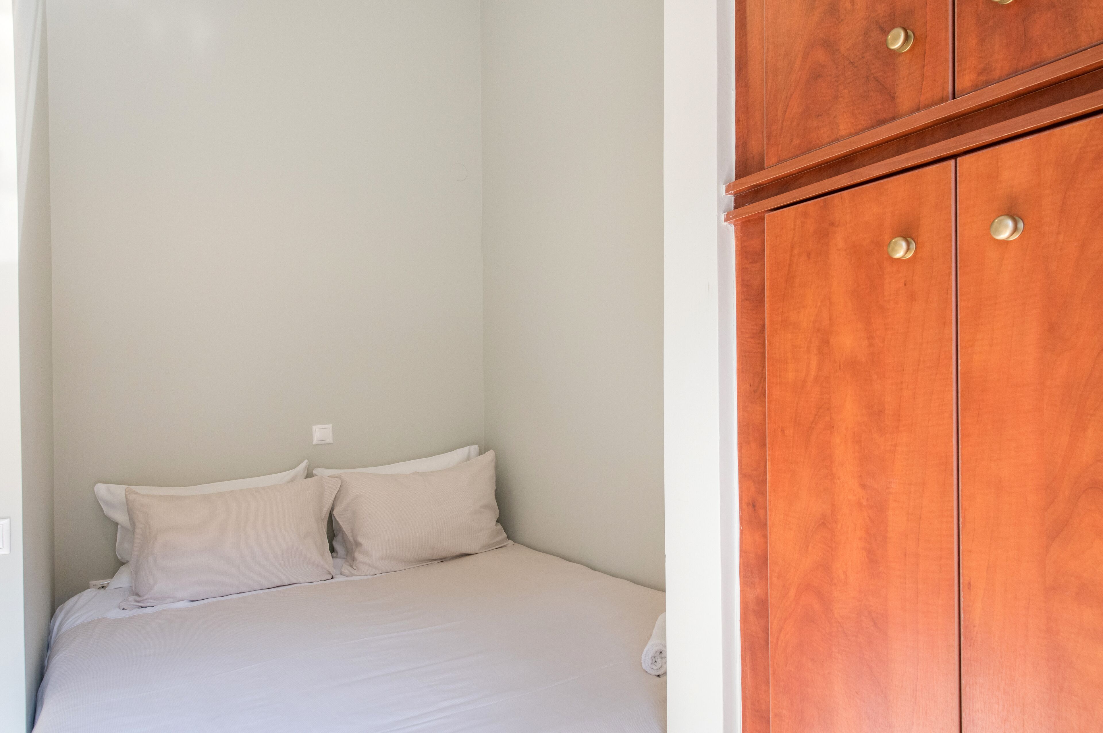 A bedroom with a bed, white pillows, and a wooden wardrobe with two doors.