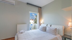 Una habitación de hotel con cama, radiador, ventana con cortinas, una silla y una lámpara.