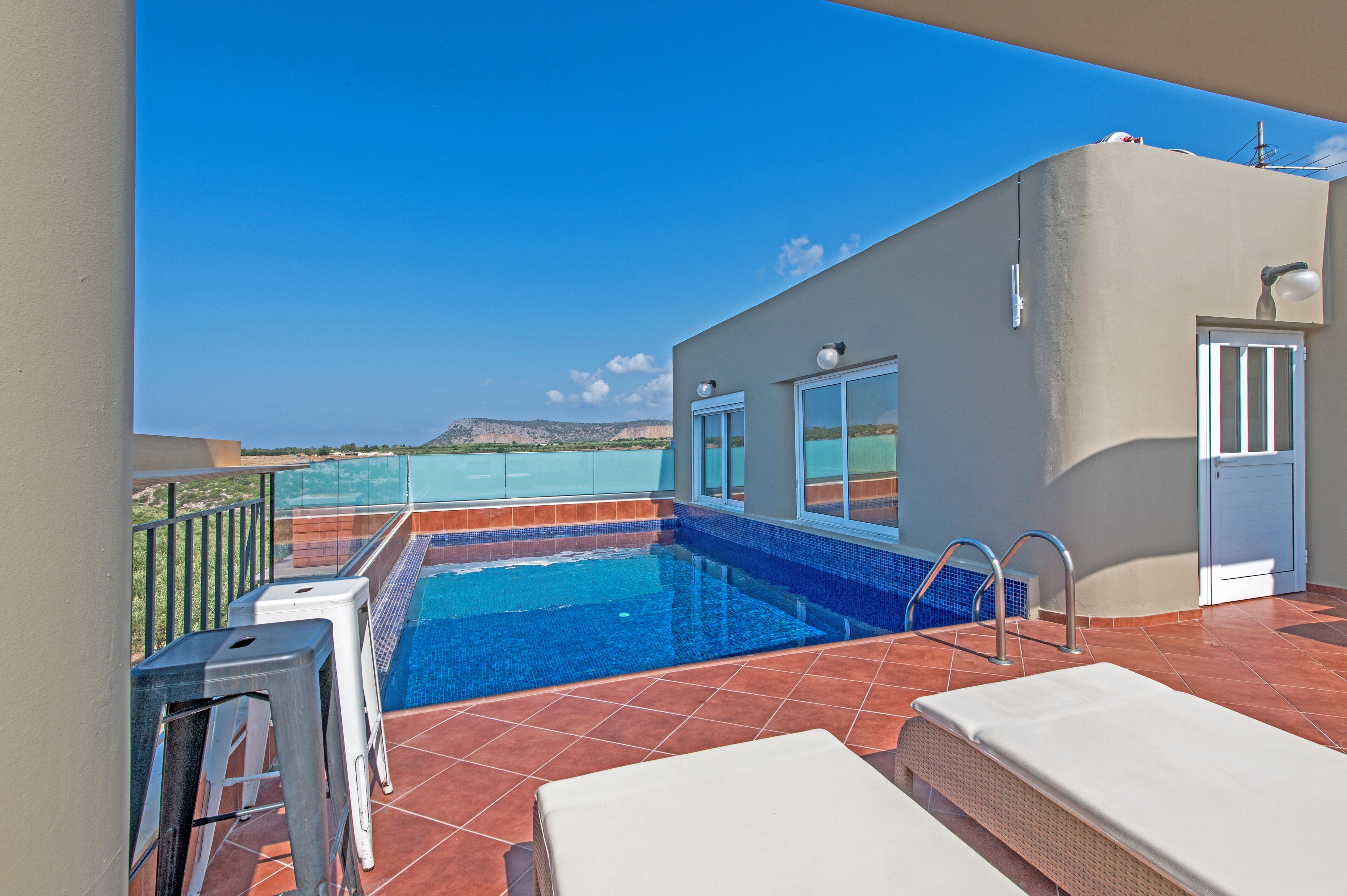 A rooftop pool with clear blue water, a view of the sea, and a modern building with large windows.