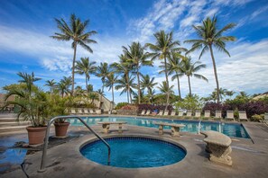 A pool area with a hot tub, lounge chairs, and palm trees.
