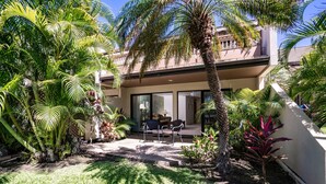 A modern house with a patio, surrounded by lush tropical plants.
