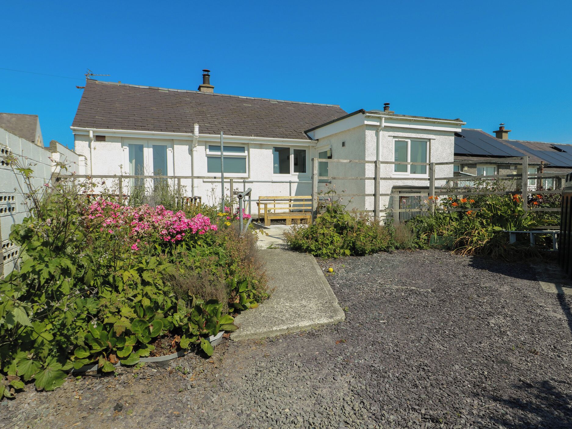 A two-story house with a gravel driveway and a garden with pink flowers.