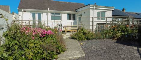 A two-story house with a gravel driveway and a garden with pink flowers.