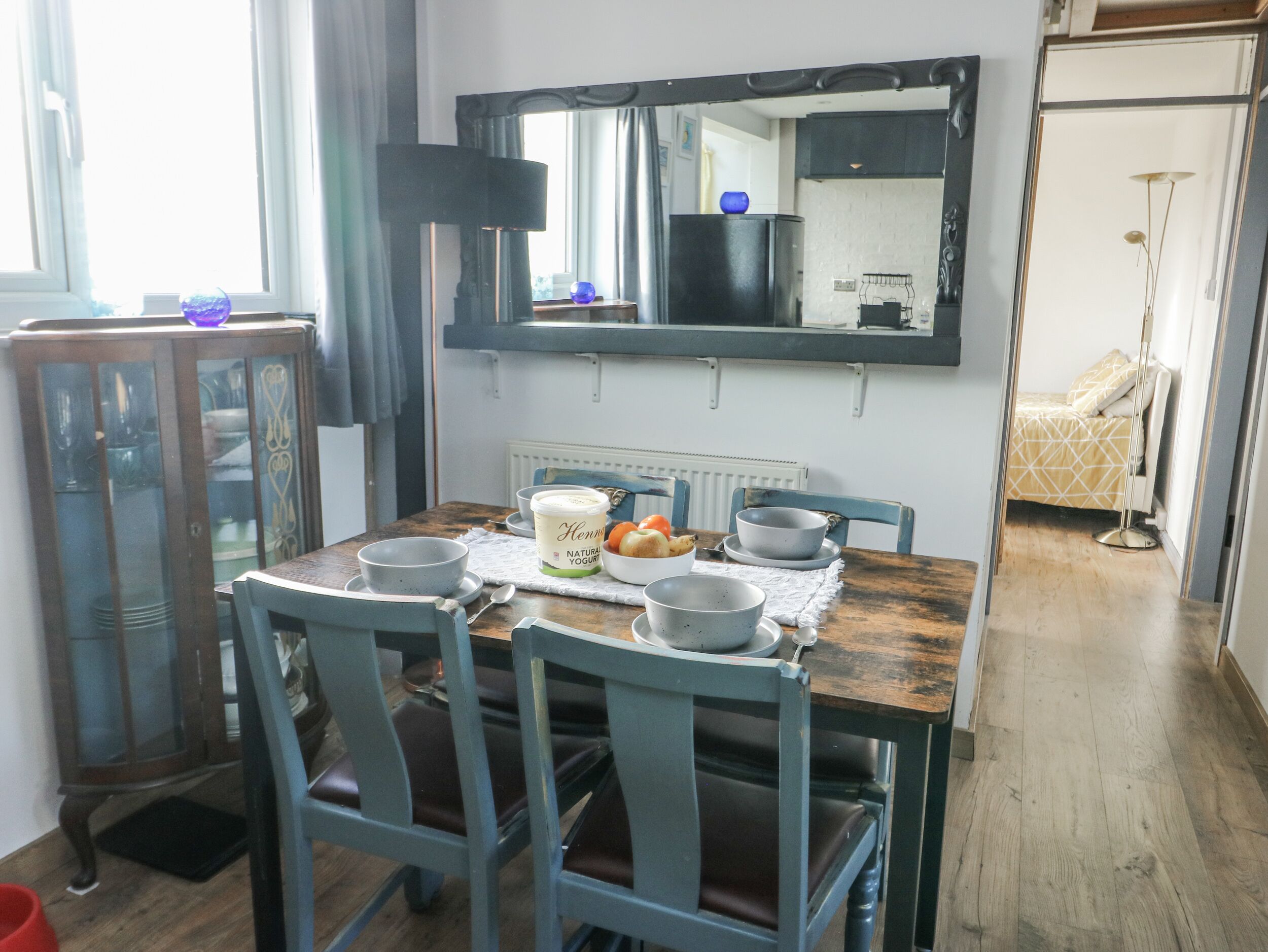 Un coin repas avec une table en bois, quatre chaises et un grand miroir au-dessus.