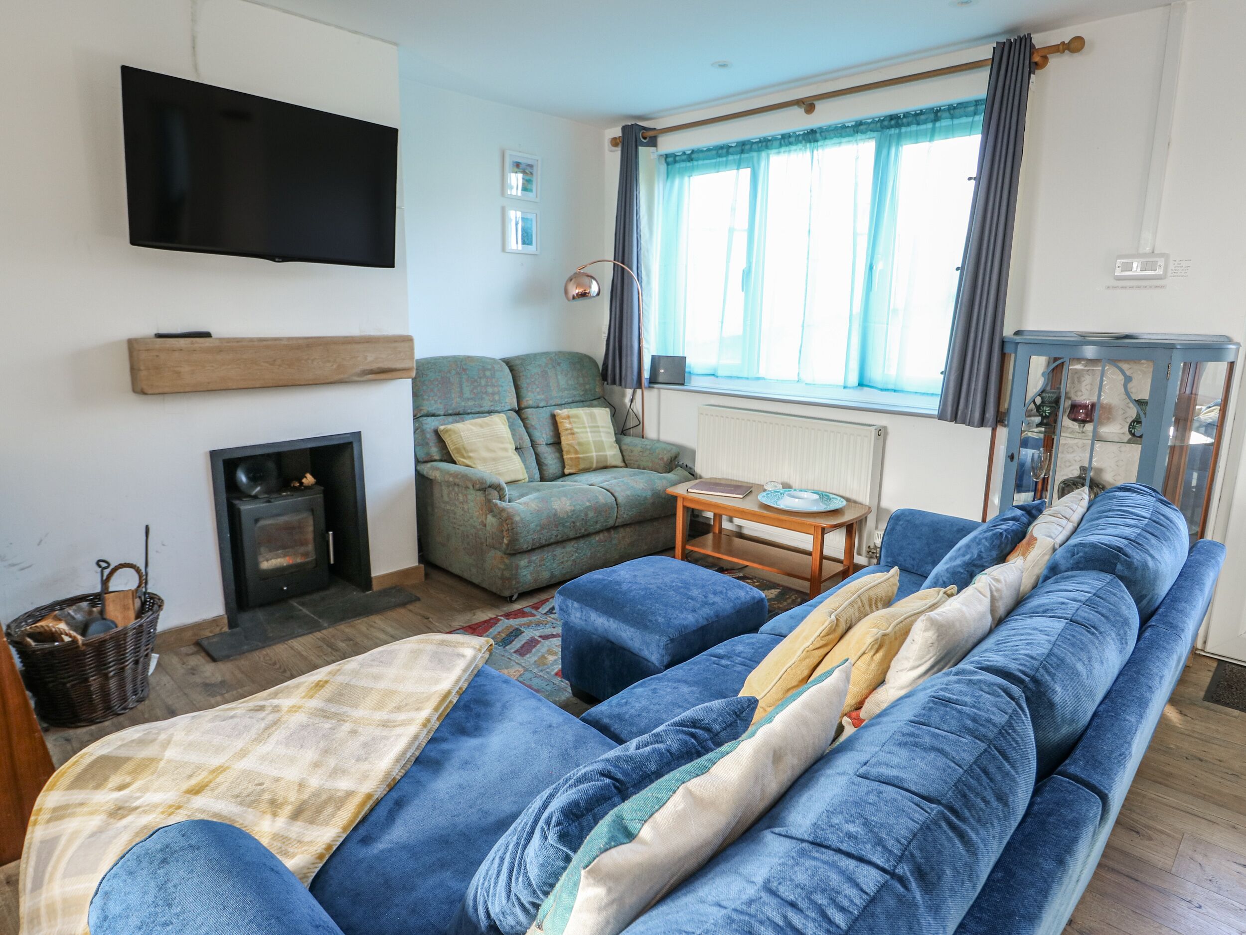 A living room with a sofa set, a television mounted on the wall, a fireplace, and a window with curtains.