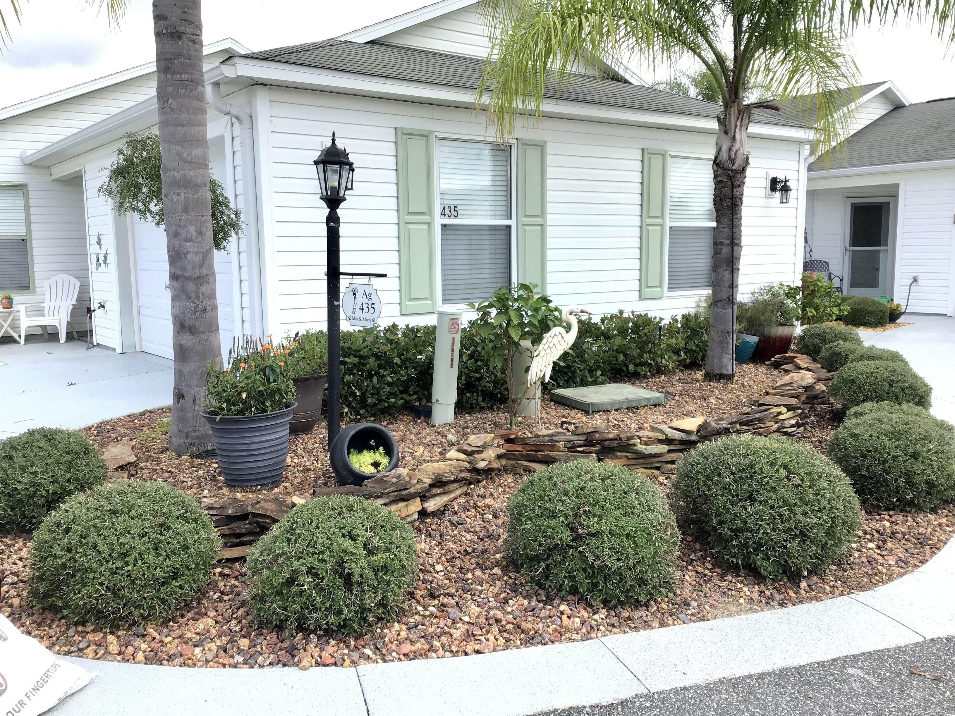A residential house with a well-maintained front yard featuring a bird sculpture, neatly trimmed bushes, and a small patio area.