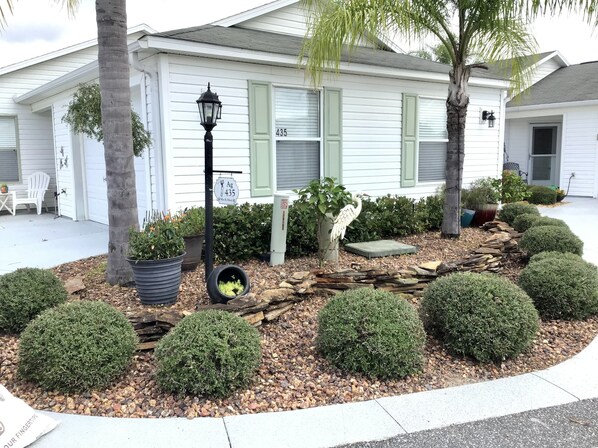 A residential house with a well-maintained front yard featuring a bird sculpture, neatly trimmed bushes, and a small patio area.