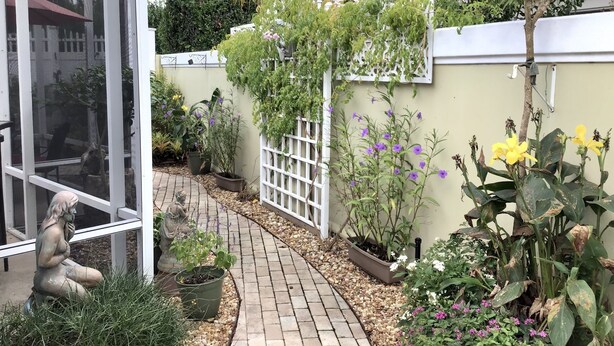 Um jardim com um caminho pavimentado, vasos de plantas e uma estátua.